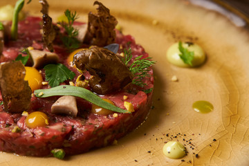 Beef tartare Steak with egg yolk, pistachios, truffle oil, green mayonnaise on porcelain plate. Classic tartare meat with ingredients. Luxury food