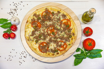 appetizing pizza with tuna, olive oil, spices and basil leaves on a white table, flat lay