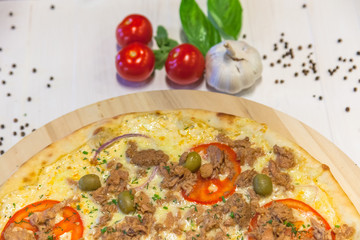 appetizing pizza with tuna, garlic and basil leaves on a white table