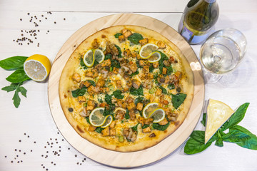 appetizing pizza with shrimps, lemon and a glass of wine on a white table, flat lay