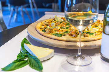 appetizing pizza with shrimps, lemon and a glass of wine on a white table