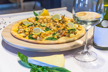 appetizing pizza with shrimps, lemon and a glass of wine on a white table