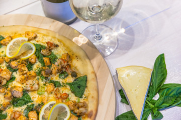 appetizing pizza with shrimps, lemon and a glass of wine on a white table