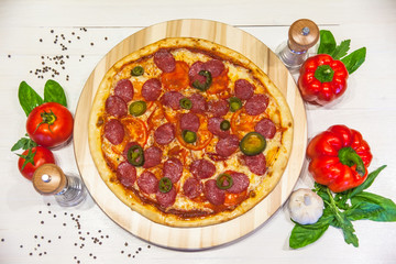 appetizing pizza with sausages and ham, spices and basil on a white table, flat lay