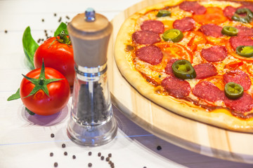 appetizing pizza with sausages and ham, spices on a white table