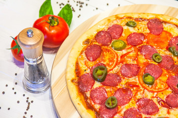 appetizing pizza with sausages and ham, spices and basil on a white table