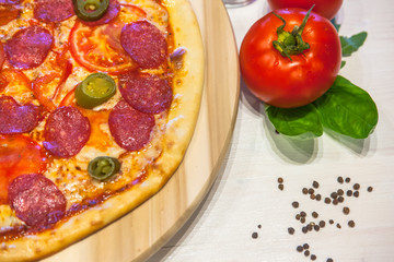 appetizing pizza with sausages and ham, spices on a white table, close up