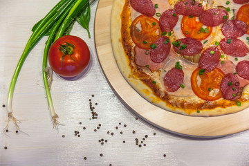 appetizing pizza with sausages and ham, spices and green onions on a white table, flat lay