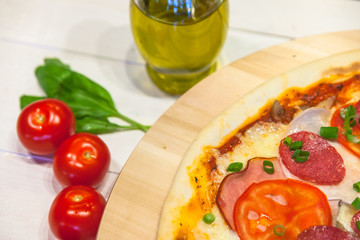 appetizing pizza with sausages and ham, olive oil and basil on a white table