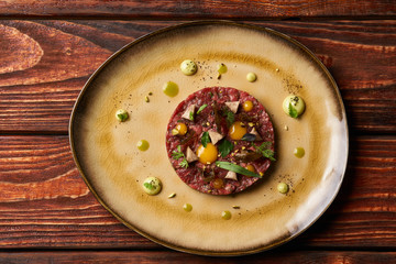 Tartare Steak with egg yolk, pistachios, truffle oil, green mayonnaise on plate and glass of red wine, served on restaurant table. Classic Beef tartare meat, Luxury food