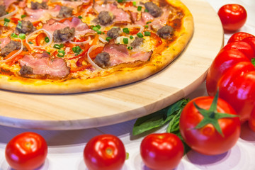 appetizing pizza with bacon, bell pepper and basil on a white table