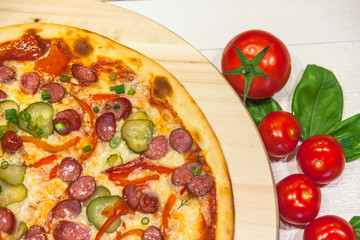 appetizing pizza with small sausages, basil and tomatoes on a white table, flat lay