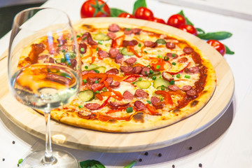 appetizing pizza with small sausages, basil, tomatoes and a glass of white wine on a white table