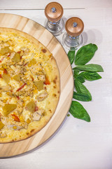 appetizing pizza with chicken and pineapple, basil and spices on a white table, flat lay