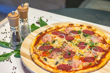 appetizing pizza with sausages, bacon, basil and spices on a white table