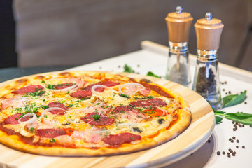 appetizing pizza with sausages, bacon, basil and spices on a white table