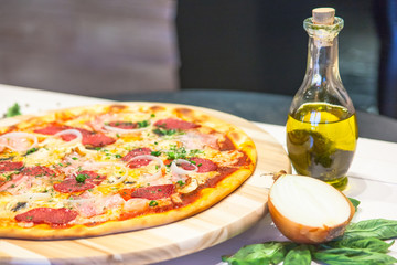 appetizing pizza with sausages, bacon, basil and olive oil on a white table