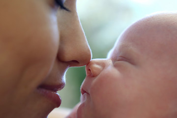 mom touches her nose on the nose of a sleeping newborn baby close-up
