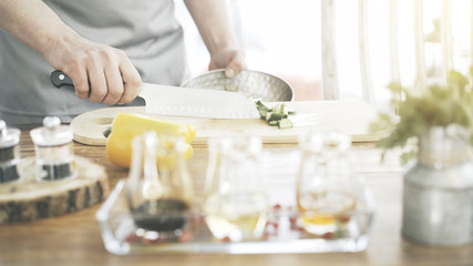 A close up of a male cooker's hands is putting chopped cucumbers to a bowl from a wooden cooking board with a large knife