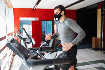 beautiful pumped up young man, engaged in sports, in training mask for breathing on the treadmill,...