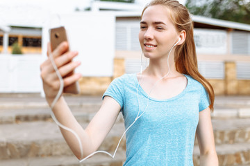 Girl athlete with a phone in her hands, running listening to music, morning training