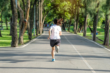 Fototapeta premium young fitness woman running in the park outdoor, female runner walking on the road outside, asian athlete jogging and exercise on footpath in sunlight morning. Sport, healthy and wellness concepts