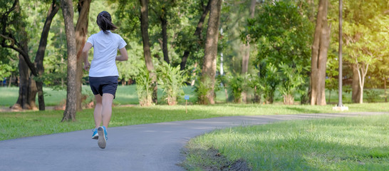 young fitness woman running in the park outdoor, female runner walking on the road outside, asian athlete jogging and exercise on footpath in sunlight morning. Sport, healthy and wellness concepts