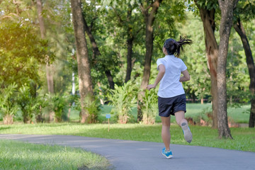 young fitness woman running in the park outdoor, female runner walking on the road outside, asian athlete jogging and exercise on footpath in sunlight morning. Sport, healthy and wellness concepts