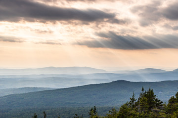 Fototapeta premium Rays of sunlight shining through clouds over rolling mountain view