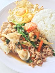 Spicy fried basil leaf and vegtable with seafood and fried egg with rice in white plate on white background. Thai style food.