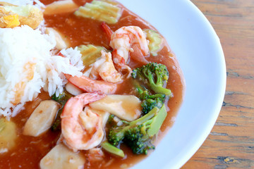 stir fried shrimp and Broccoli in thai red curry paste sauce with rice, Curry fried shrimps and cooked rice in white dish closeup on wooden table. Thai style food.