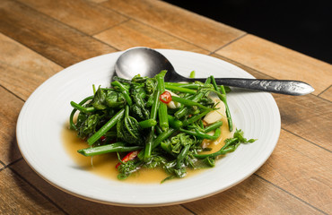 Stir Fried Water Spinach or Vietnamese fried morning glory, rau muong xao toi on white dish on wood table.