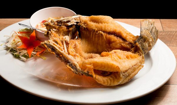 Deep fried fish with fish sauce serve with mango sauce in white dish on wood table.
