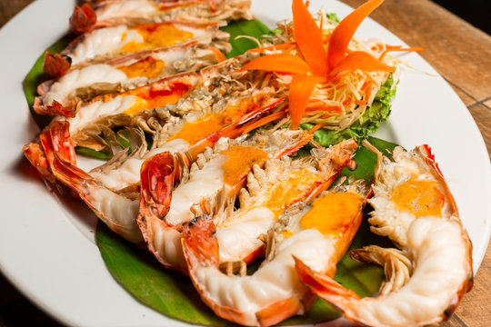 Grilled shrimp with Shrimp Paste in white dish showing the delicious Shrimp Paste inside its shell on wood table. Thai seafood.