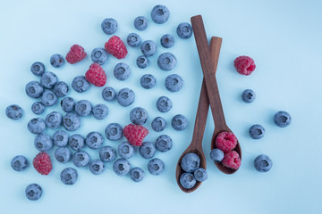 Blueberies and raspberries in wooden spoons on blue background