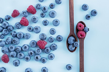 Blueberies and raspberries in wooden spoons on blue background