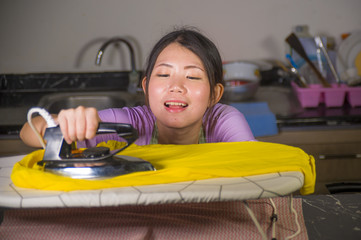young pretty and happy Asian Korean woman using iron at home kitchen ironing clothes smiling cheerful and carefree enjoying domestic chores