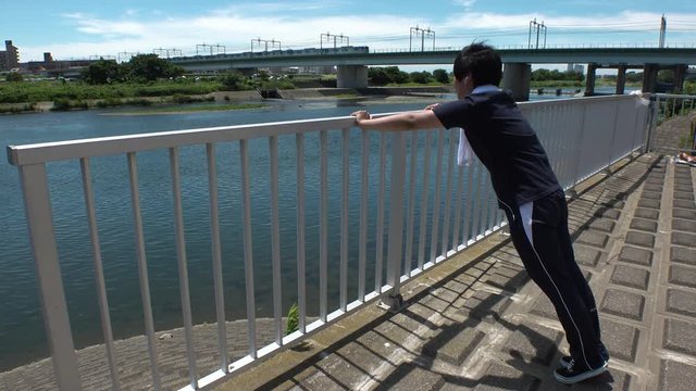 Young JAPANESE RUNNER MAN doing push ups at the riverside of Tama river in Tokyo.