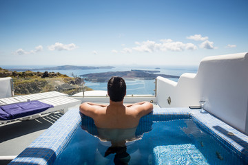 Dark haired man relaxing and contemplating beautiful scene from private pool in one of Oia,...