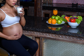 Portrait of pregnant mother drinking milk  with fruits background.