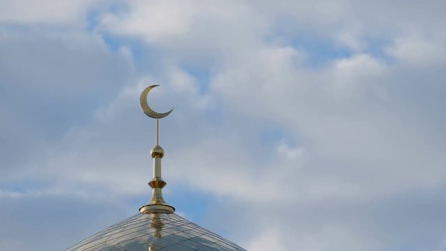 Time Lapse. The golden crescent on the minaret of the Islamic mosque on a heavenly blue background with white clouds. Close up.