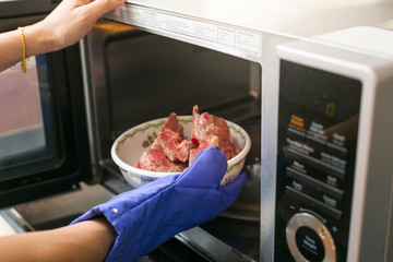 Woman putting grilled pork into microwave oven. inside view