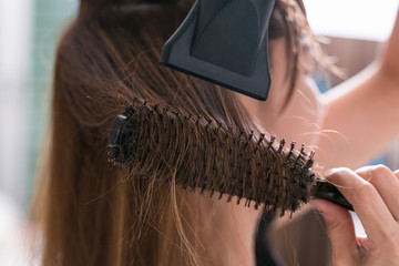 Drying blond hair with hair dryer and round brush.