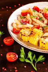 Italian traditional cuisine. Penne pasta with tomato sauce and tomatoes, with parsley and grilled corn. Background image on a wooden table. copy space, top view