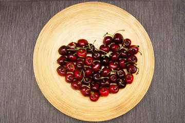 red and Burgundy cherry is laid out in the shape of a heart on a wooden plate