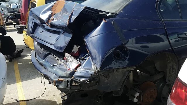 Slow moving footage of a smashed up blue car with broken tail-light filmed in a junkyard.