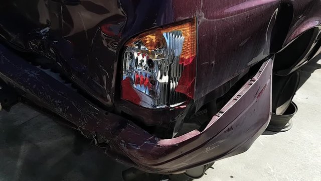 Slow moving footage of a smashed up purple car with a broken tail-light filmed in a junkyard.