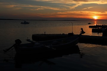 Sunset above Adriatic sea molo with visible silhouettes of fishing boats, one with light for night fishing