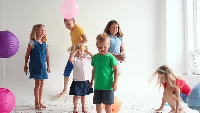 Group of  7 seven children play with air balloons, confetti in light room on birthday party