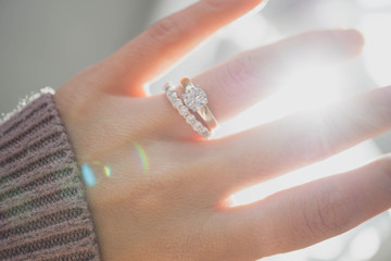 Close up of elegant diamond ring on woman finger with dark pink sweater winter clothe and sunlight tone. love and wedding concept.soft and selective focus.